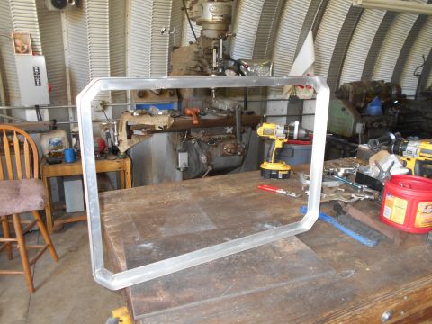 1992 Ford Bronco - A metal frame sits on a workbench, surrounded by tools and industrial equipment.