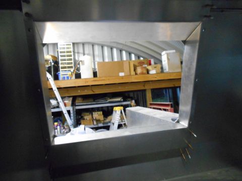 1992 Ford Bronco - View from inside a metal structure looking out into a cluttered workshop area with storage shelves and equipment.