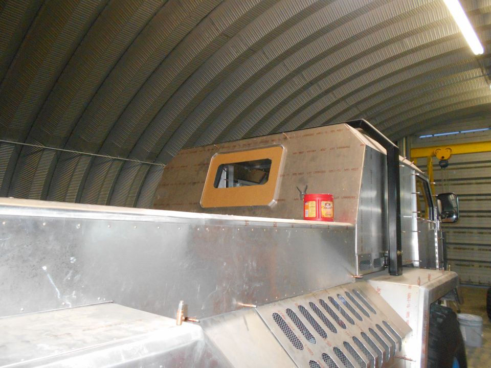 Custom truck build in garage with metal body panels and a small window. Red cans on shelf
