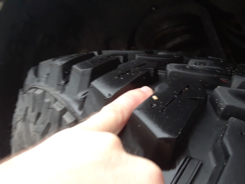 Close-up of a tire tread with a finger pointing at it. Supermotors.net logo in corner