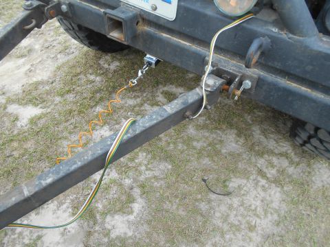 1992 Ford Bronco - Close-up view of a trailer hitch assembly, showing the safety cable and electrical wiring connected to the vehicle's rear bumper.