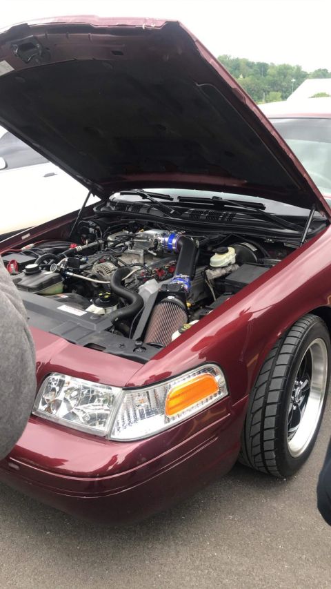 2004 Ford Crown Victoria - The engine bay of a maroon Ford Crown Victoria is visible with the hood open, revealing the engine and aftermarket modifications.