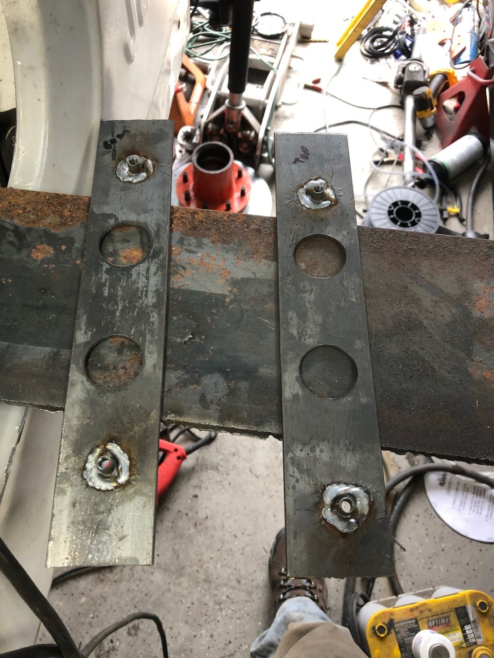 Two metal plates with welded nuts and circular cutouts on a rusty frame.