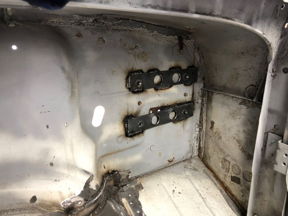 Welded metal brackets with holes on the interior of a vehicle undergoing restoration.