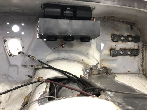 1992 Jeep Wrangler - The interior of a vehicle shows a black HVAC unit mounted to the firewall, with cables and wiring running below it. Welded metal brackets a…