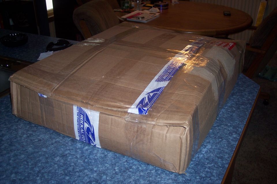 Cardboard box with RockAuto tape, wrapped in plastic, on a blue surface.
