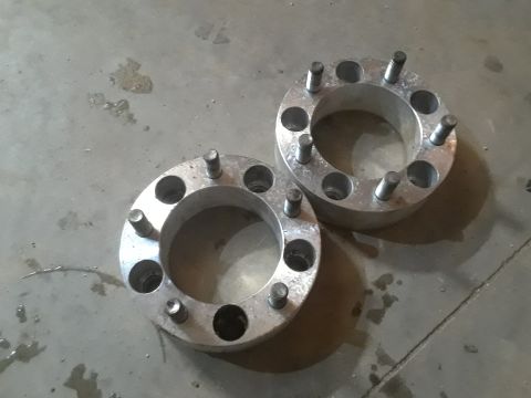 1994 Ford Bronco - Two silver wheel spacers with studs are laid out on a concrete floor with some water stains.