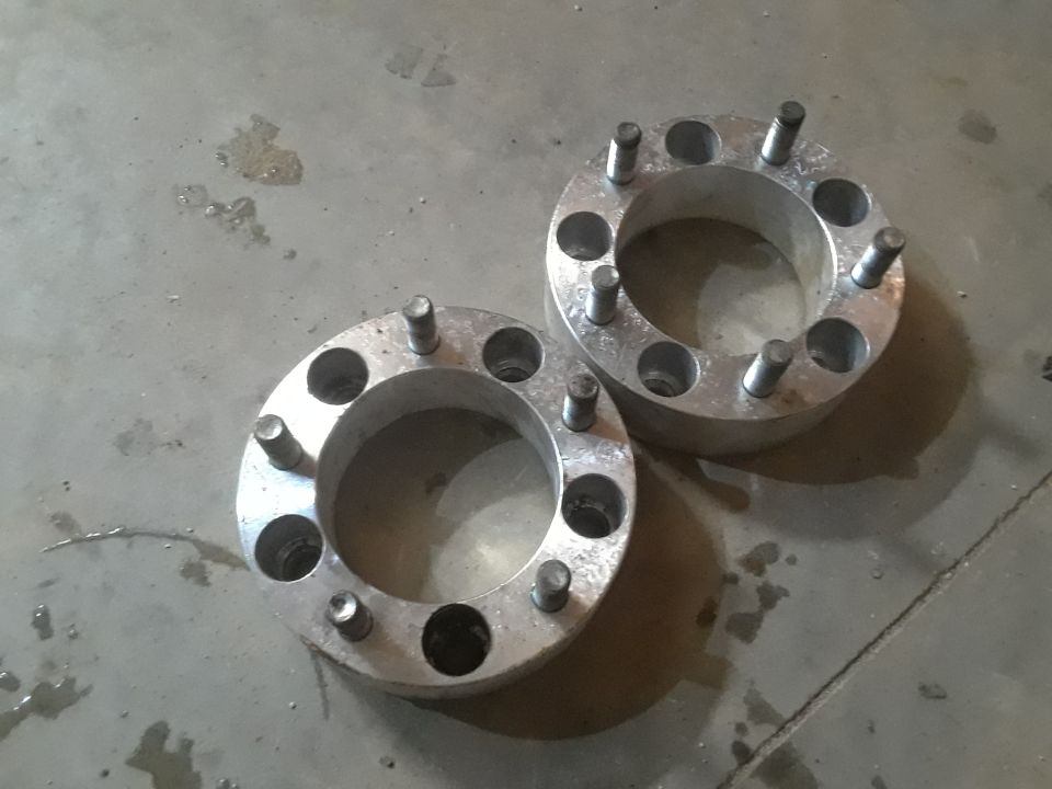 Two silver wheel spacers with studs on a concrete floor.