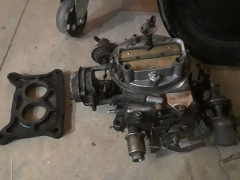 1994 Ford Bronco - A disassembled carburetor and intake manifold adapter are shown on a concrete floor. The carburetor is silver and black with various linkag…