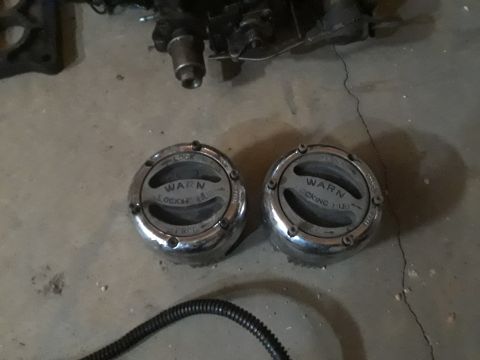 1994 Ford Bronco - Two chrome Warn locking hubs are shown on a concrete floor, possibly in a garage. The hubs have "WARN LOCKING HUB" printed on them and are…
