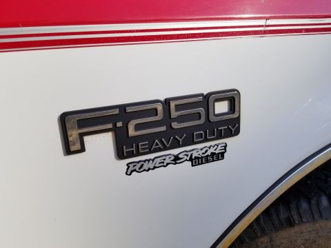 1997 Ford F-250 - A close-up of the "F250 HEAVY DUTY POWER STROKE DIESEL" badge on the side of a white truck with a red and white pinstripe detail along the…