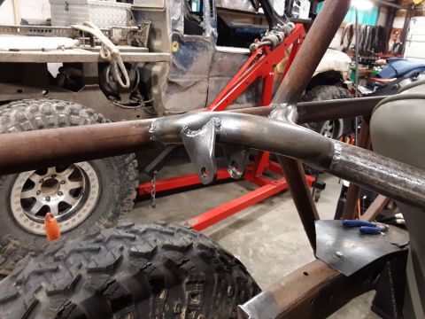 1985 Toyota Hilux - A close-up view of a custom roll cage being welded onto a vehicle frame, with large off-road tires visible in the foreground and a blue uti…