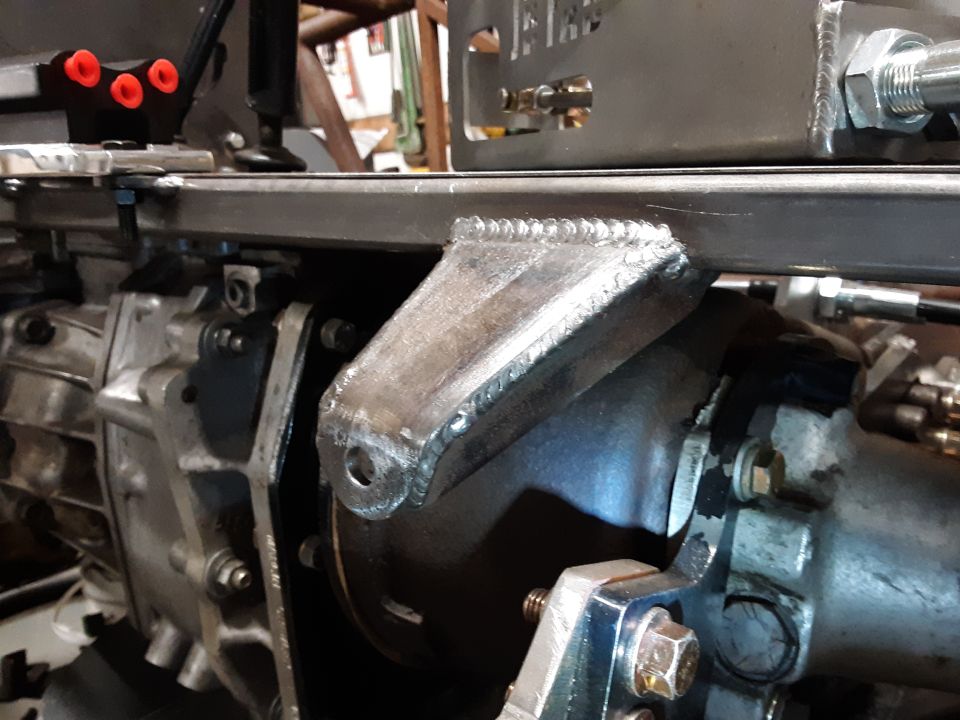 Custom welded metal bracket attached to a transmission housing.