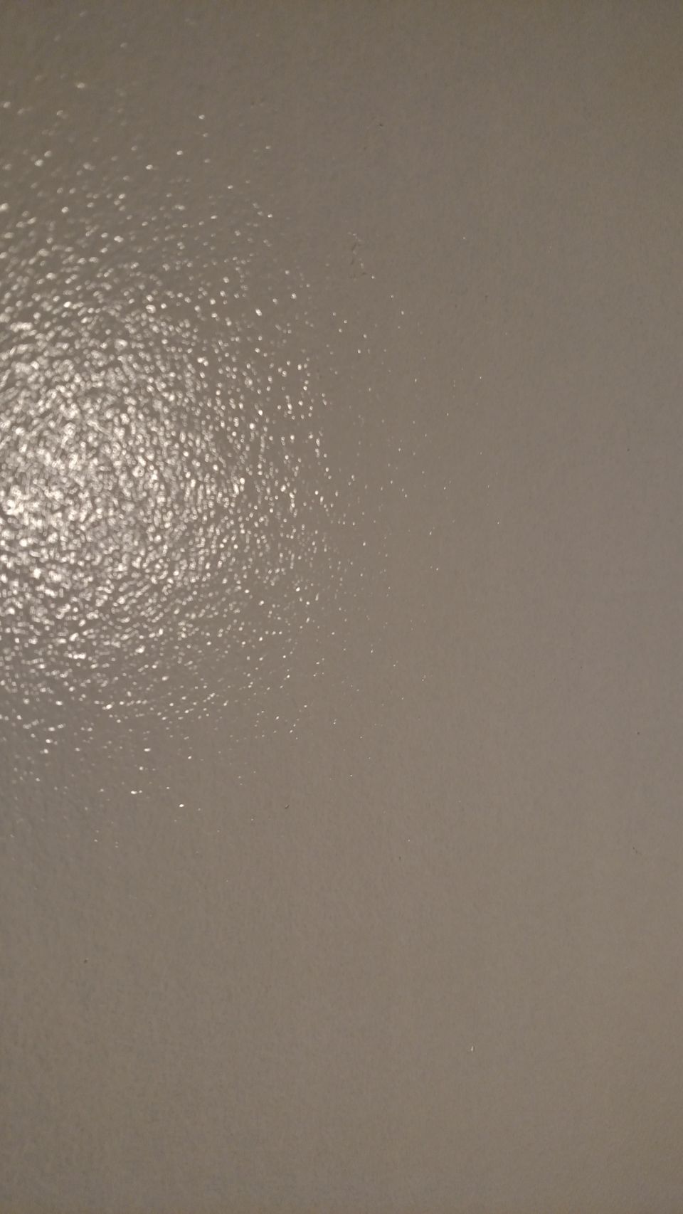 Close-up of a textured, glossy light gray surface with reflective highlights.