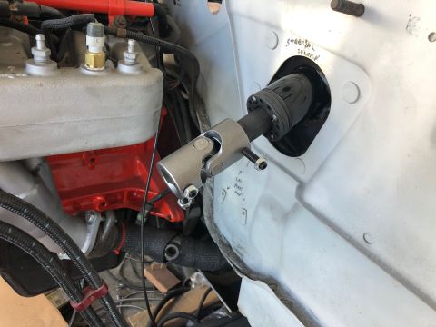 1992 Jeep Wrangler - A close-up view of a steering column U-joint assembly connected to a steering shaft passing through a firewall. The assembly is silver meta…