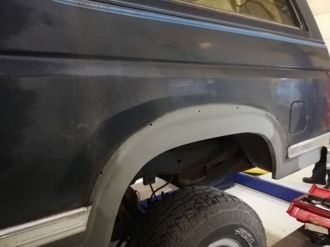 1996 Ford Bronco - Close-up view of the rear fender and wheel well of a dark blue SUV, with primer on the fender flare.
