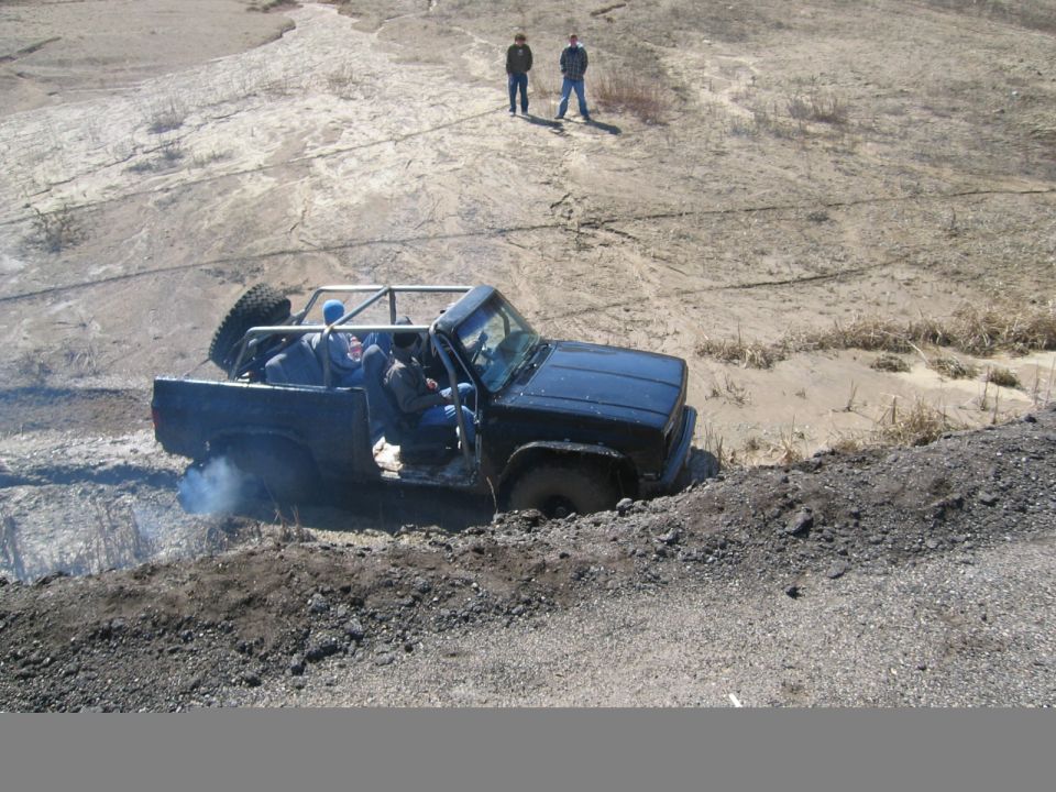 Black topless SUV with roll cage climbing a dirt hill off-road as two onlookers watch