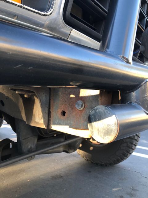 1981 Ford Bronco - Close-up view of the front bumper and frame of a dark SUV, showing some rust on the frame components.