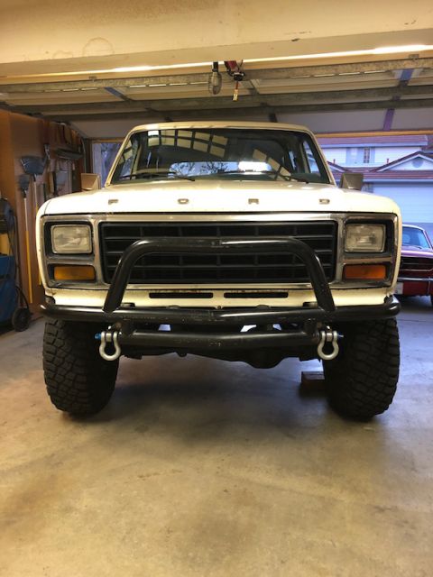 1981 Ford Bronco - Front view of a white Ford Bronco with a black bull bar and large tires, parked indoors.