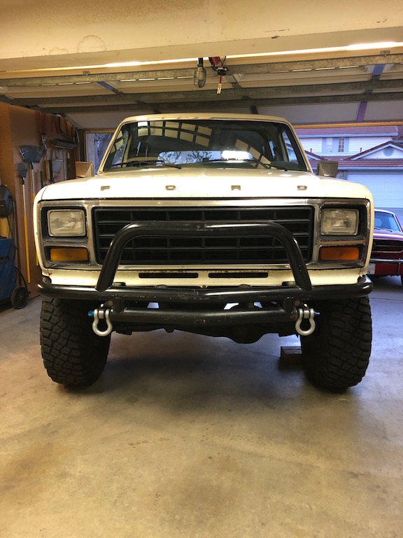White Ford Bronco with bull bar and tow hooks parked in a garage