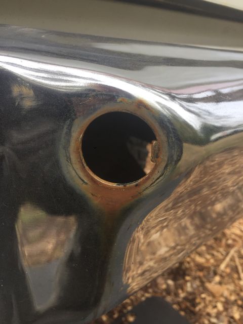 1979 Ford Bronco - Detail of a rusted fuel filler opening on a vehicle's bumper.