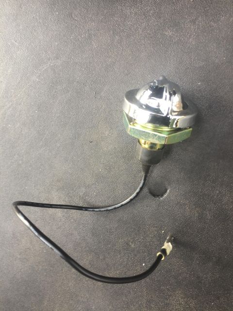 1979 Ford Bronco - A chrome dome light switch with a black wire and connector is shown against a textured gray background.
