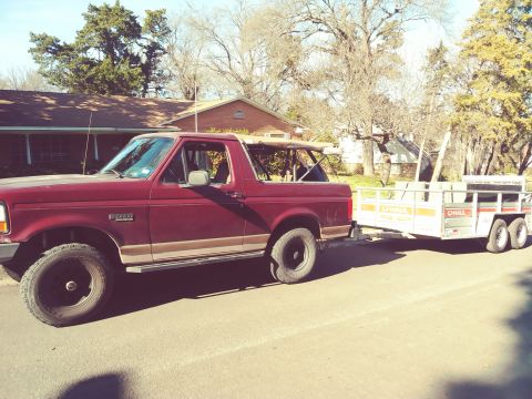 1996 Ford Bronco - A red 1996 Ford Bronco is seen from the side, towing a U-Haul trailer on a sunny day.