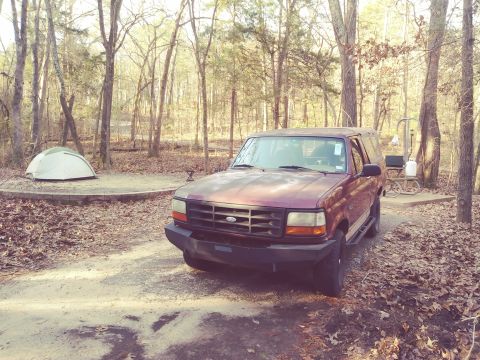 1996 Ford Bronco - A maroon Ford Bronco is parked at a campsite with a tent set up nearby.