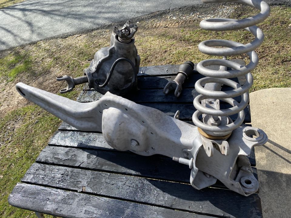 Front suspension components including control arm, differential, and coil spring laid out on a table