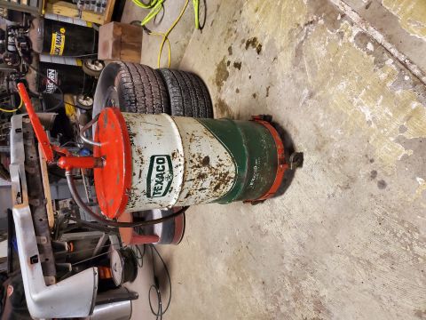 2004 Aston Martin Virage - Vintage Texaco oil drum with pump, tires, and car bumper in a garage setting.