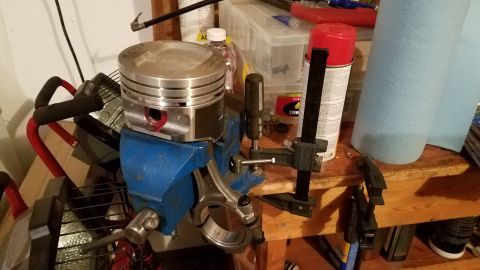 1985 Ford Bronco - Engine piston and connecting rod assembly held in a vise on a workbench.
