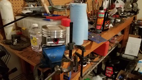 1985 Ford Bronco - A workbench is cluttered with automotive parts, tools, and cleaning supplies, suggesting a repair or maintenance session.