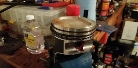 1985 Ford Bronco - A close-up of a piston, likely for engine repair, is secured in a vise on a cluttered workbench.