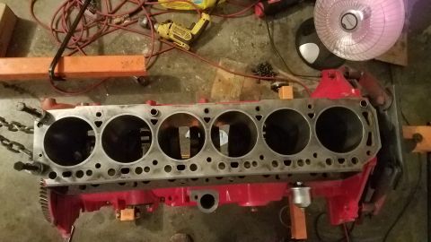 1985 Ford Bronco - Engine block with six cylinders, red painted block, and metal chains attached, likely for repair or rebuild.