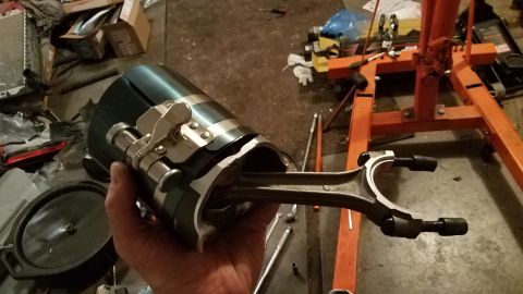 1985 Ford Bronco - A hand holds a piston ring compressor tool with a connecting rod inside, in a workshop setting.