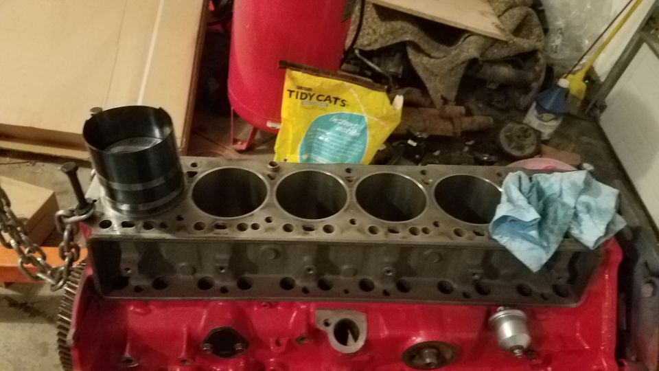 Engine block with five cylinders and a piston ring compressor tool on top. A bag of Tidy Cats litter is in the background