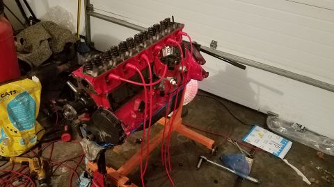 1985 Ford Bronco - A red V8 engine is mounted on an orange stand, likely undergoing repair or rebuild in a garage setting.