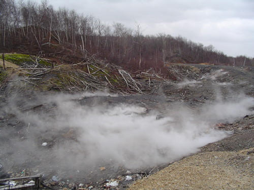 Desolate landscape with steam rising from the ground and trees in the background