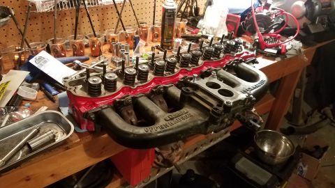 1985 Ford Bronco - Close-up of an Offenhauser intake manifold and cylinder head, likely for engine repair, resting on a workbench.