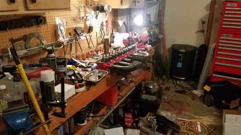 1985 Ford Bronco - A workbench is covered in tools and engine parts, suggesting a repair or rebuilding process is in progress.