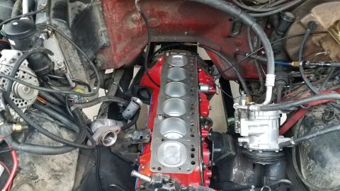 1985 Ford Bronco - Engine bay with disassembled engine block, revealing cylinders and gasket. Various hoses and wires are present.