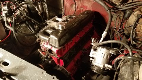 1985 Ford Bronco - A close-up view of a red engine block with a black valve cover and intake manifold, situated in an engine bay with various hoses and electr…