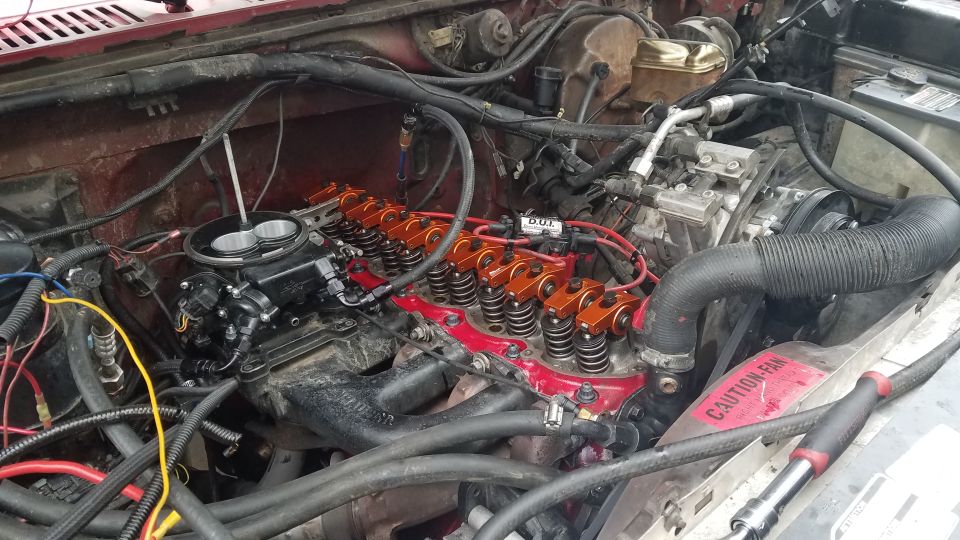 Red Ford Bronco engine bay with orange roller rockers and black carburetor.