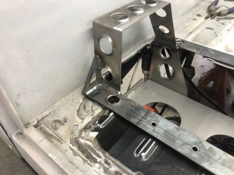 1992 Jeep Wrangler - A custom metal bracket with circular cutouts is being welded to the floor of a vehicle. The bracket appears to be part of a fabrication pro…