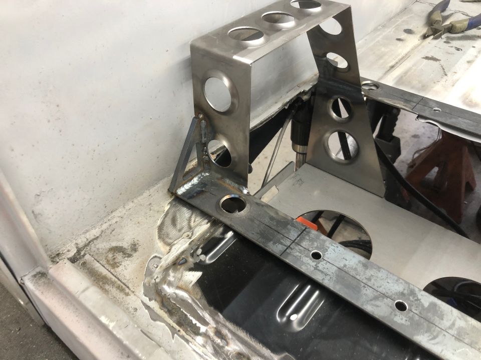 Custom metal bracket with holes being welded to a vehicle floor.