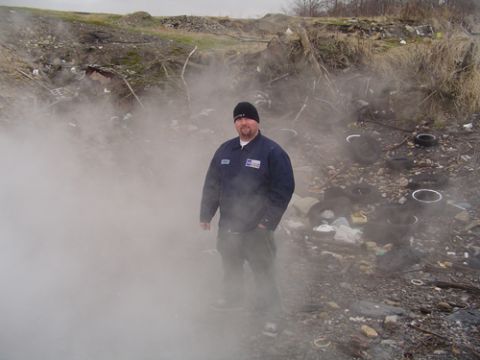 1979 Ford Bronco - A man stands in a junkyard surrounded by steam and debris.