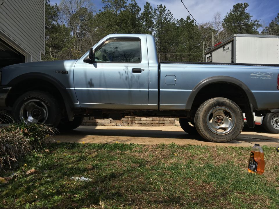 Light blue 1998 Ford Ranger pickup truck, side view, parked in driveway with trailer.