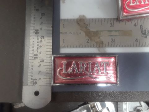 1994 Ford Bronco - A close-up of a red and silver "LARIAT" emblem is shown next to a ruler. The emblem is rectangular with a metallic red background and silve…