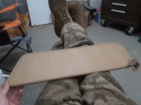 1994 Ford Bronco - A tan sun visor is held in front of the viewer's legs, which are covered in camouflage pants. The visor has a metal bracket on the right si…