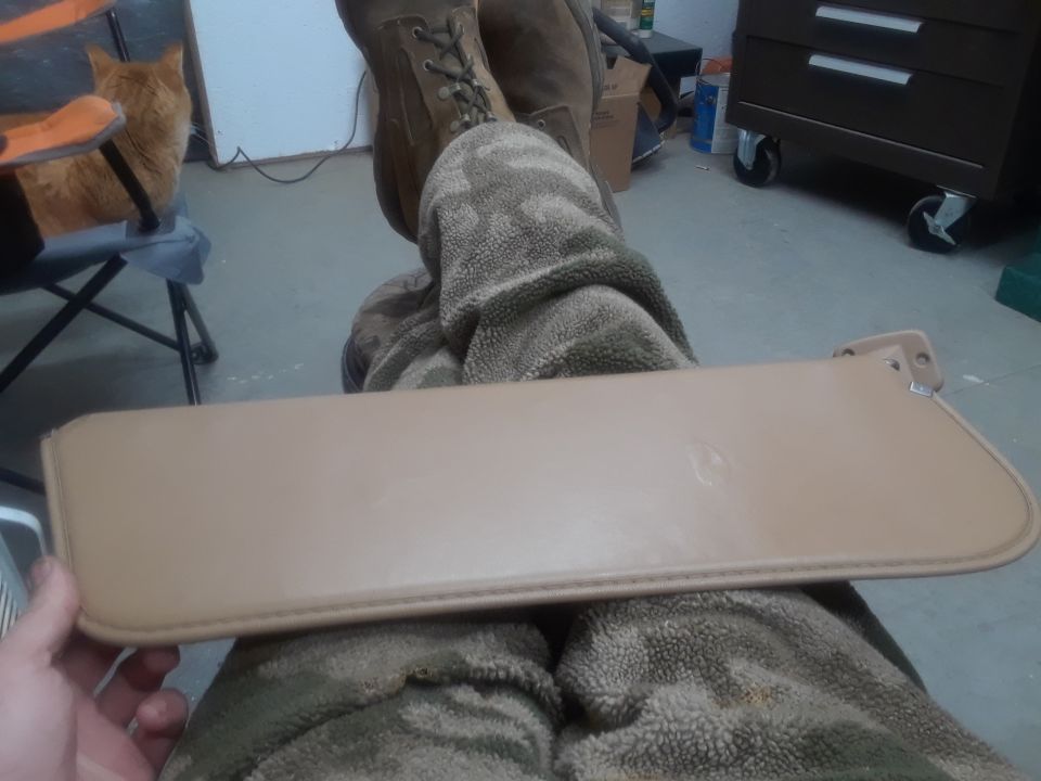 Tan sun visor held in front of person in camouflage pants and boots.